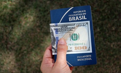 Woman holding Brazilian passport with 100 dollars banknote on top of it. Brazilians traveling to United States concept. 