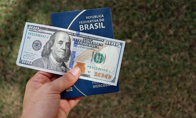 Woman holding Brazilian passport with 100 dollars banknote on top of it. Brazilians traveling to United States concept. 