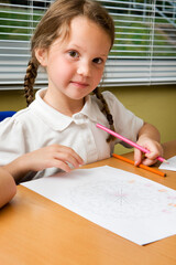 Elementary School: Young Artist. A look to the camera from a young primary school girl sitting at her desk in the classroom working on an art project.