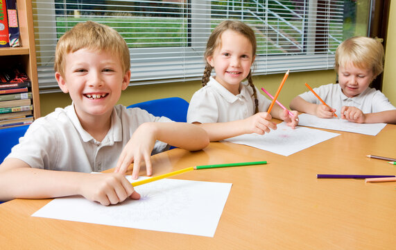 Elementary School: Pupils working together. Bright smiles and eye contact from a small friendly group of junior school friends working together at a shared desk in their classroom.
