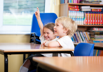 Elementary School: Eager Pupils. A pair of eager primary school pupils sitting at a desk in a classroom eager to be involved with the lesson.