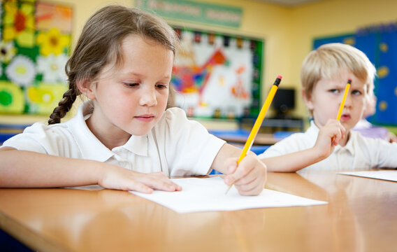 Elementary School: Creative Writing. A young primary school girl concentrating on her writing exercise while at her desk in the classroom.