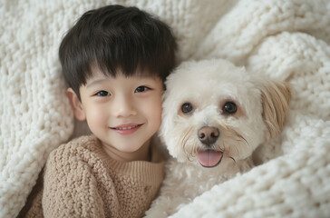 A joyful little boy and his cheerful dog cuddle together under a soft blanket in their cozy home. The warmth of the moment reflects their strong bond and happiness shared.