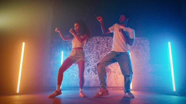 Rehearsing contemporary choreography in dance studio with vibrant atmosphere. Full-length portrait of two African dancers performing modern and ethnic dance movements synchronously, slow motion shot