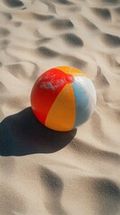 Obraz premium Colorful beach ball resting on sandy shoreline near ocean waves