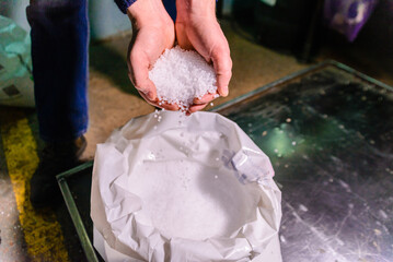 White plastic grains and polymer granules, with a hand holding polymer pellets. Represents raw...