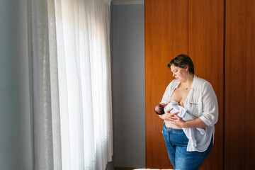Mother breastfeeding newborn son in bedroom