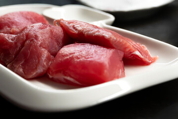 Sliced raw tuna fish on white rectangular plate on black table, fish steaks close-up