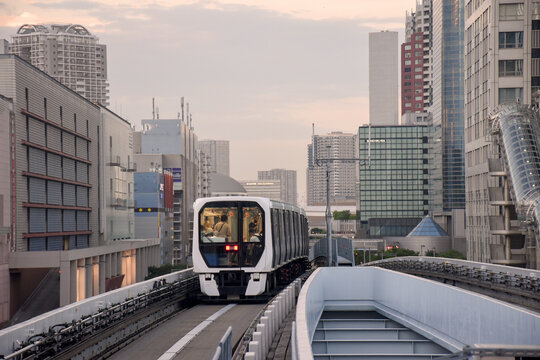 A modern monorail glides through Tokyo's urban landscape, surrounded by high-rise buildings during a serene evening.