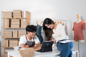 A woman is pointing at a document while discussing work with a man on a laptop, with clothing racks...