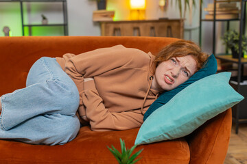Sick ill woman suffering from period cramps, painful stomach ache lying on sofa in living room at...