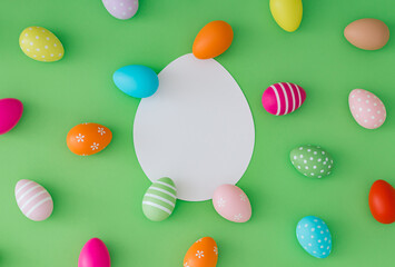 Spring pattern made of colorful Easter eggs on pastel green background with paper card note copy space. Minimal Easter concept. Creative festive holiday layout. Easter aesthetic. Flat lay.