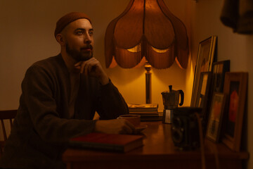 A man sitting at a desk with a cup of coffee indoors lit by a warm light.