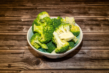 Fresh broccoli pieces in bowl on wooden table