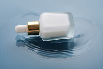 Bottle with white moisturizing serum in water on blue background.