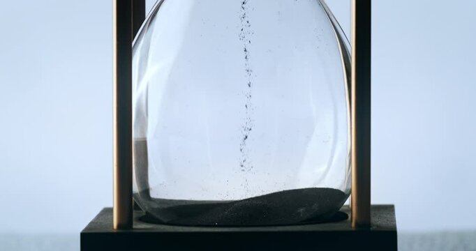 Super slow motion macro of fluid flow of black sand grains particles running inside hourglass sandglass clepsydra measuring passing time in countdown to deadline at 1000 fps.