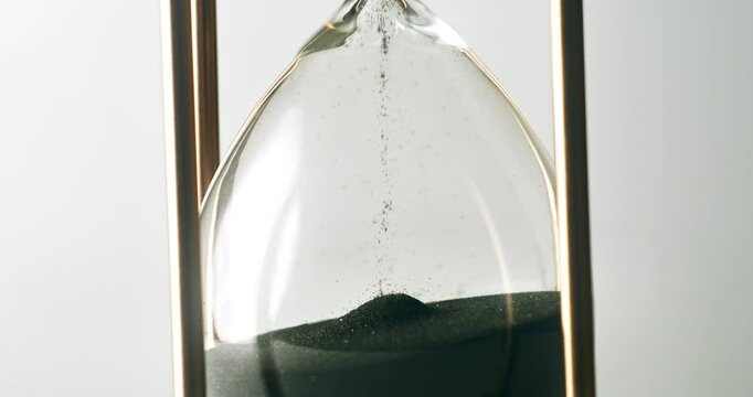 Super slow motion macro of fluid flow of black sand grains particles running inside hourglass sandglass clepsydra measuring passing time in countdown to deadline at 1000 fps.