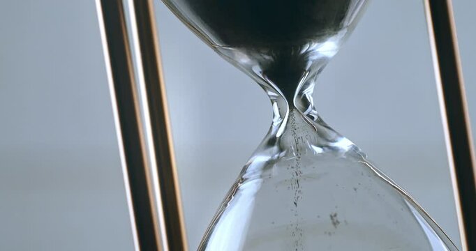 Super slow motion macro of fluid flow of black sand grains particles running inside hourglass sandglass clepsydra measuring passing time in countdown to deadline at 1000 fps.