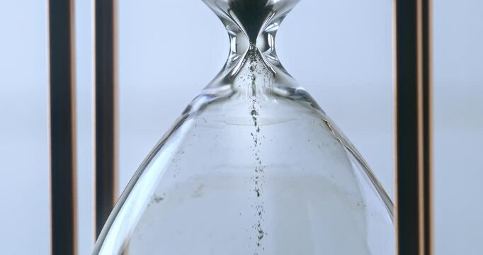 Super slow motion macro of fluid flow of black sand grains particles running inside hourglass sandglass clepsydra measuring passing time in countdown to deadline at 1000 fps.