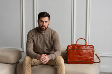 A man is comfortably sitting on a sofa, with a leather orange briefcase