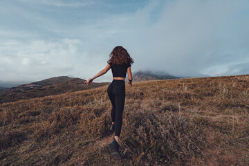 Young woman running away in the mountains in cloudy weather