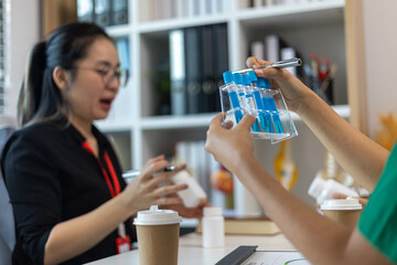 A woman and a man are sitting at a desk with a laptop and a notebook. The woman is wearing a blue shirt and a red lanyard. The man is holding a pen
