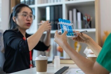 A woman and a man are sitting at a desk with a laptop and a notebook. The woman is wearing a blue shirt and a red lanyard. The man is holding a pen
