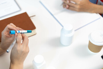 A woman and a man are sitting at a desk with a laptop and a notebook. The woman is wearing a blue shirt and a red lanyard. The man is holding a pen
