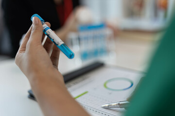 A woman is holding two blue tubes and a syringe. She is in a green shirt. The tubes are filled with a blue liquid

