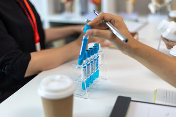 A woman is holding two blue tubes and a syringe. She is in a green shirt. The tubes are filled with a blue liquid

