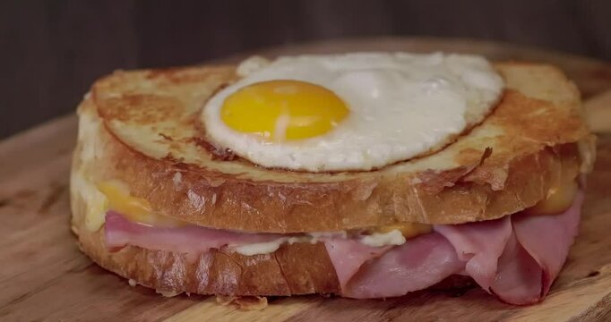 Croque Madame or Grilled cheese with ham and egg on a wooden cutting board. The sandwich is toasted and has a runny yolk