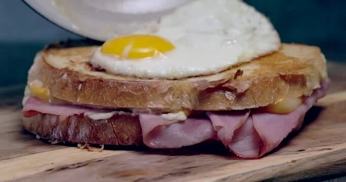 Croque Madame or Grilled cheese with ham and egg on a wooden cutting board. The sandwich is toasted and has a runny yolk