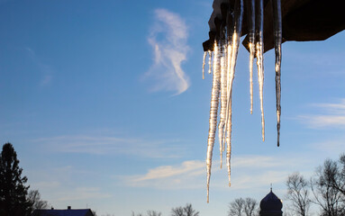 On a beautiful sunny winter day, ice icicles hang from the roof of a house. The icicles are long,...
