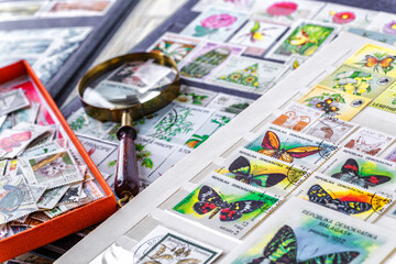 Philately.Collection of stamps and magnifying glass.Postage stamps range with different species of butterflies.A page of storage book album for storing old postage stamps.