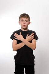 A young boy stands against a plain white backdrop, arms crossed across his chest. His expression is...