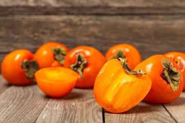 Persimmon on textured wooden background. Persimmon fruit. A piece of ripe, juicy, sweet persimmon fruit. Vegan. Orchard. Close-up. Space for text. Copy space.