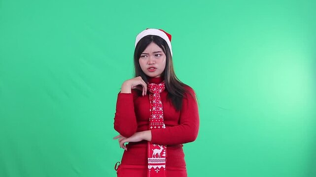 Asian girl wearing Christmas sweater, Santa hat and scarf, showing talkative expression with both hands gesture as if talking continuously on green background, green screen.