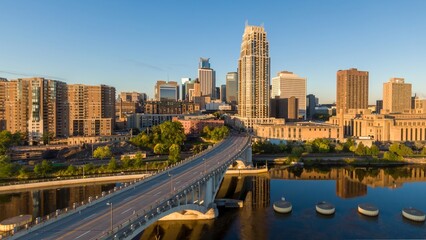 Sunrise over Minneapolis skyline, reflecting on the river. City buildings, bridge, and calm water....