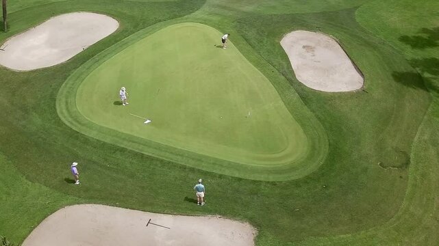 Aerial circling helicopter shot of team of four playing golf 