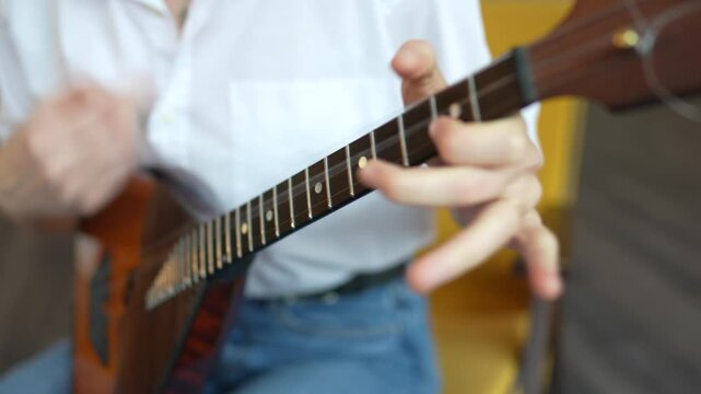 Girl playing acoustic balalaika swiftly with plucking motion at home. Create home music, classic and ethnic musical instruments, practicing memorizing frets and strum. High angle view