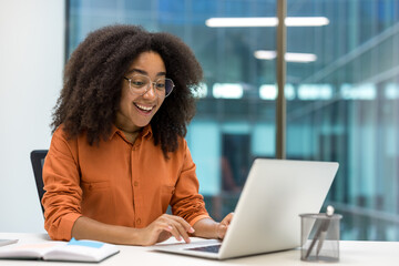 Young happy satisfied businesswoman working with laptop inside office at workplace, joyful office worker woman typing on keyboard smiling.