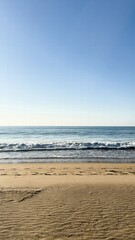 Waves gently roll onto a serene beach under clear skies in a coastal location during the day