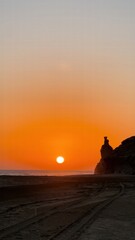 Obraz premium Sunset over the ocean near rocky cliffs with vibrant orange and yellow hues creating a picturesque scene