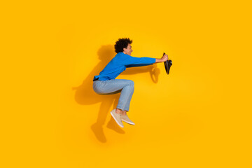 Full body photo of attractive young man jump sit hold steering wheel dressed stylish blue clothes isolated on yellow color background