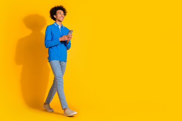 Full size photo of nice young man hold smart phone walk empty space isolated on yellow color background © deagreez