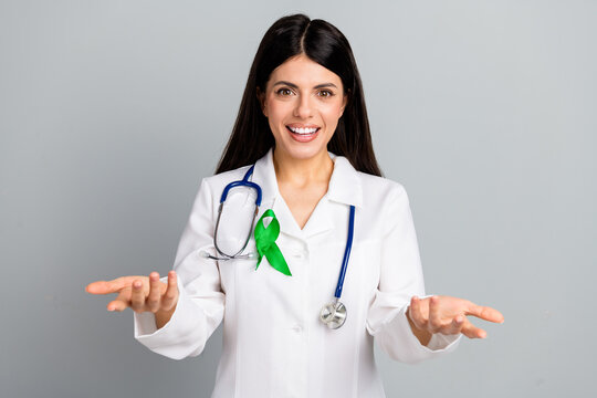 Smiling female doctor with green ribbon in medical uniform on gray background, promoting health awareness and treatment