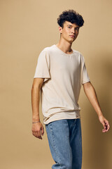 Casual young man in a light beige t shirt and blue jeans against a plain beige background, exuding a relaxed and modern style, perfect for fashion related concepts