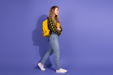 Young woman in a casual outfit walking with a yellow backpack and notebook on purple wall