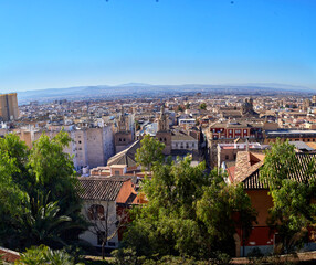 Obraz premium Granada cityscape with historic architecture; rooftops, church towers, and greenery in the foreground; mountains visible on the horizon;