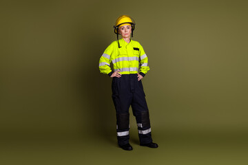 Confident middle-aged woman in high-visibility uniform and helmet standing against a khaki background